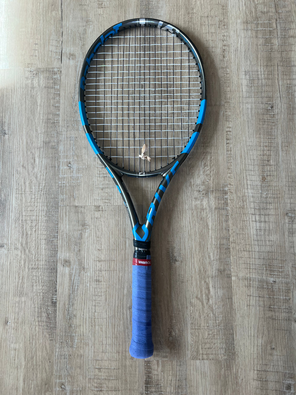 A pre-owned Babolat Pure Drive VS tennis racket (4 3/8 grip) lies on a wooden floor, ideal for advanced players.