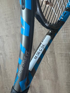 A close-up of a pre-owned Babolat Pure Drive VS 4 3/8 tennis racquet, ideal for advanced players, featuring a white sticker marked "M 56 C 54" on the frame.
