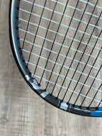 Close-up of a pre-owned Babolat Pure Drive VS (4 3/8) tennis racquet's head, showcasing its strings and frame on a light wood floor—engineered for precision, power, and spin.