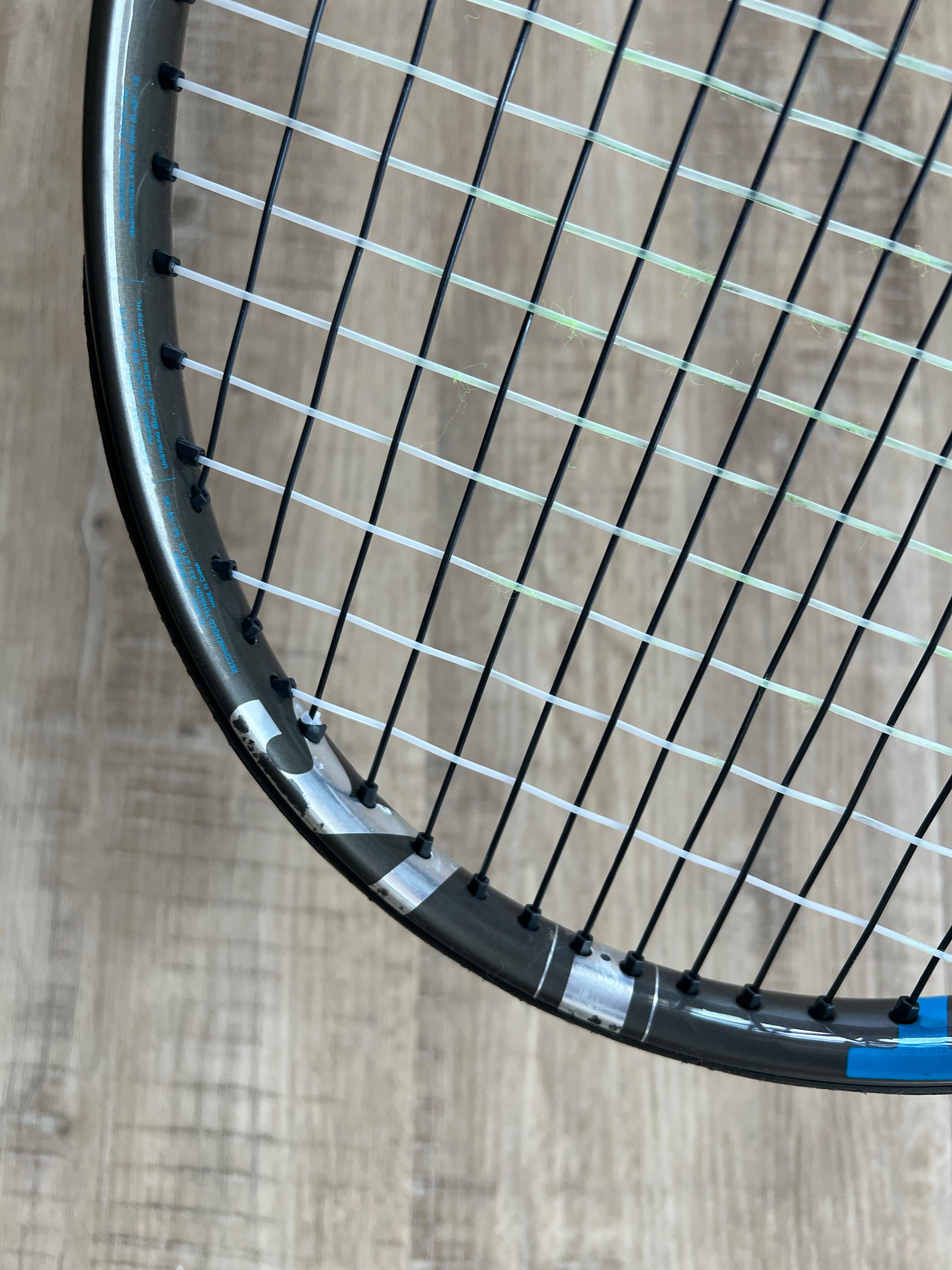 Close-up of a pre-owned Babolat Pure Drive VS (4 3/8) tennis racquet's head, showcasing its strings and frame on a light wood floor—engineered for precision, power, and spin.