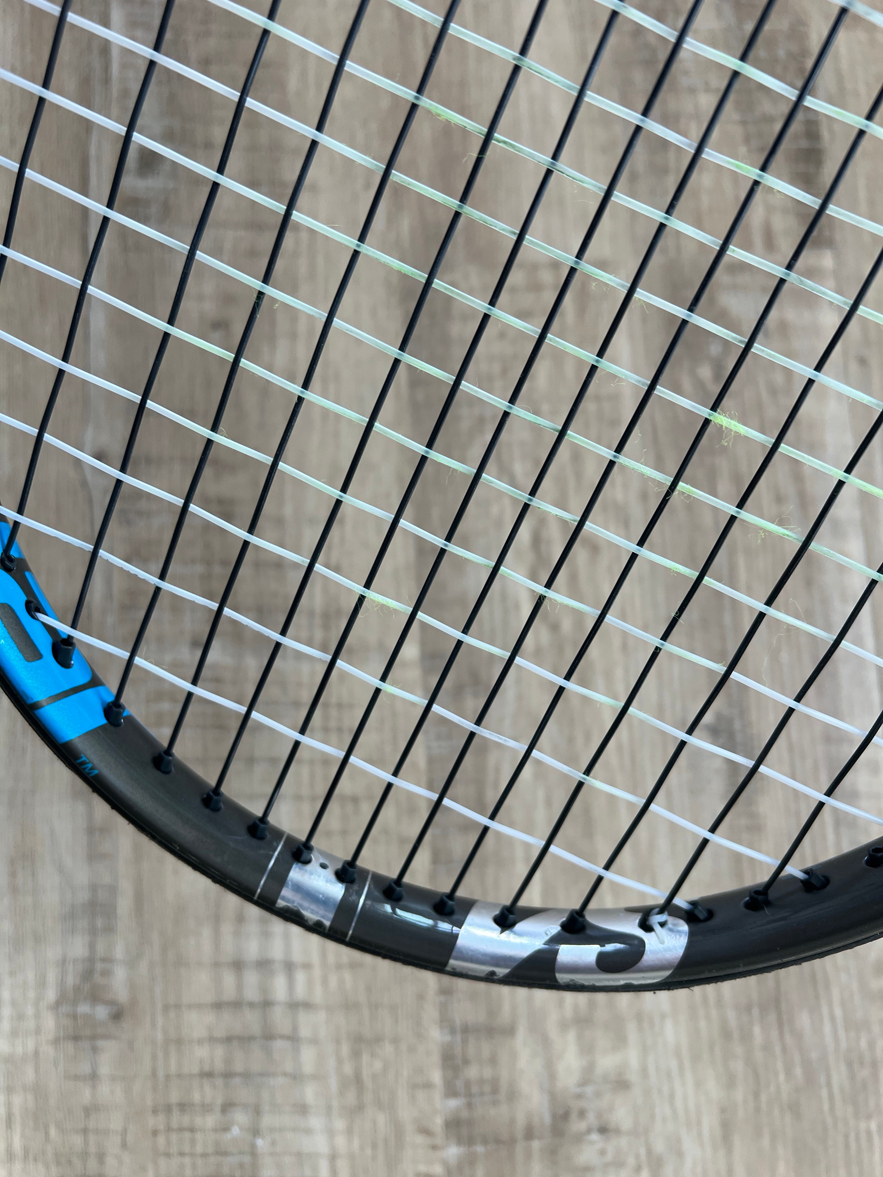 Close-up of a pre-owned Babolat Pure Drive VS (4 3/8) tennis racquet with black and white strings on a wooden floor, ideal for players seeking power and spin.