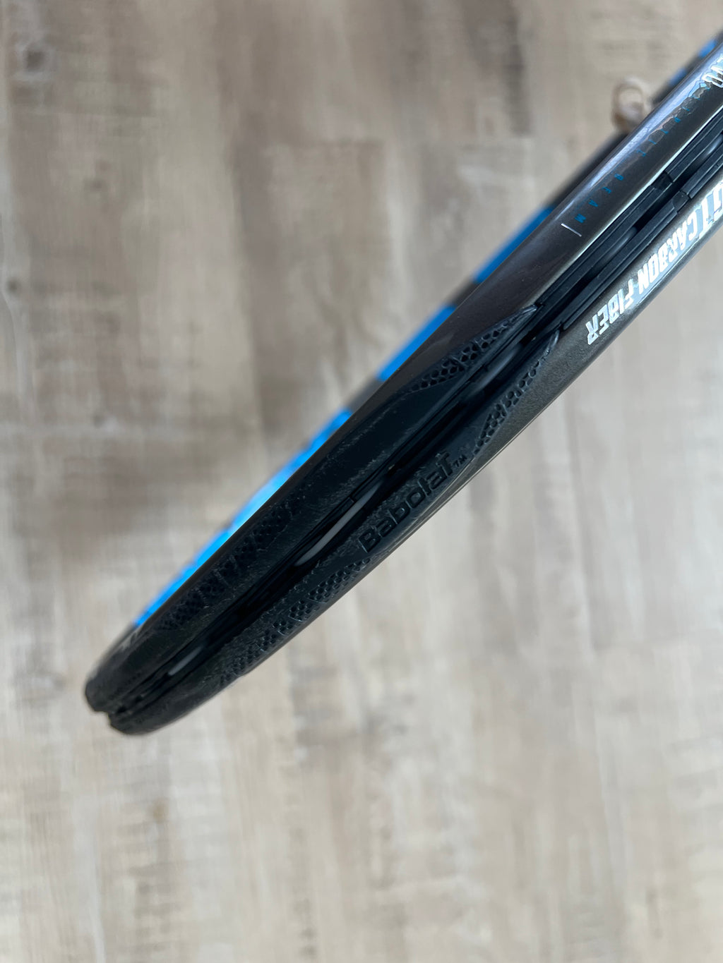 Close-up of a "Pasela" tire on a rim against a wood floor—crafted with precision like a pre-owned Babolat Pure Drive VS (4 3/8), a racquet renowned for power and spin.
