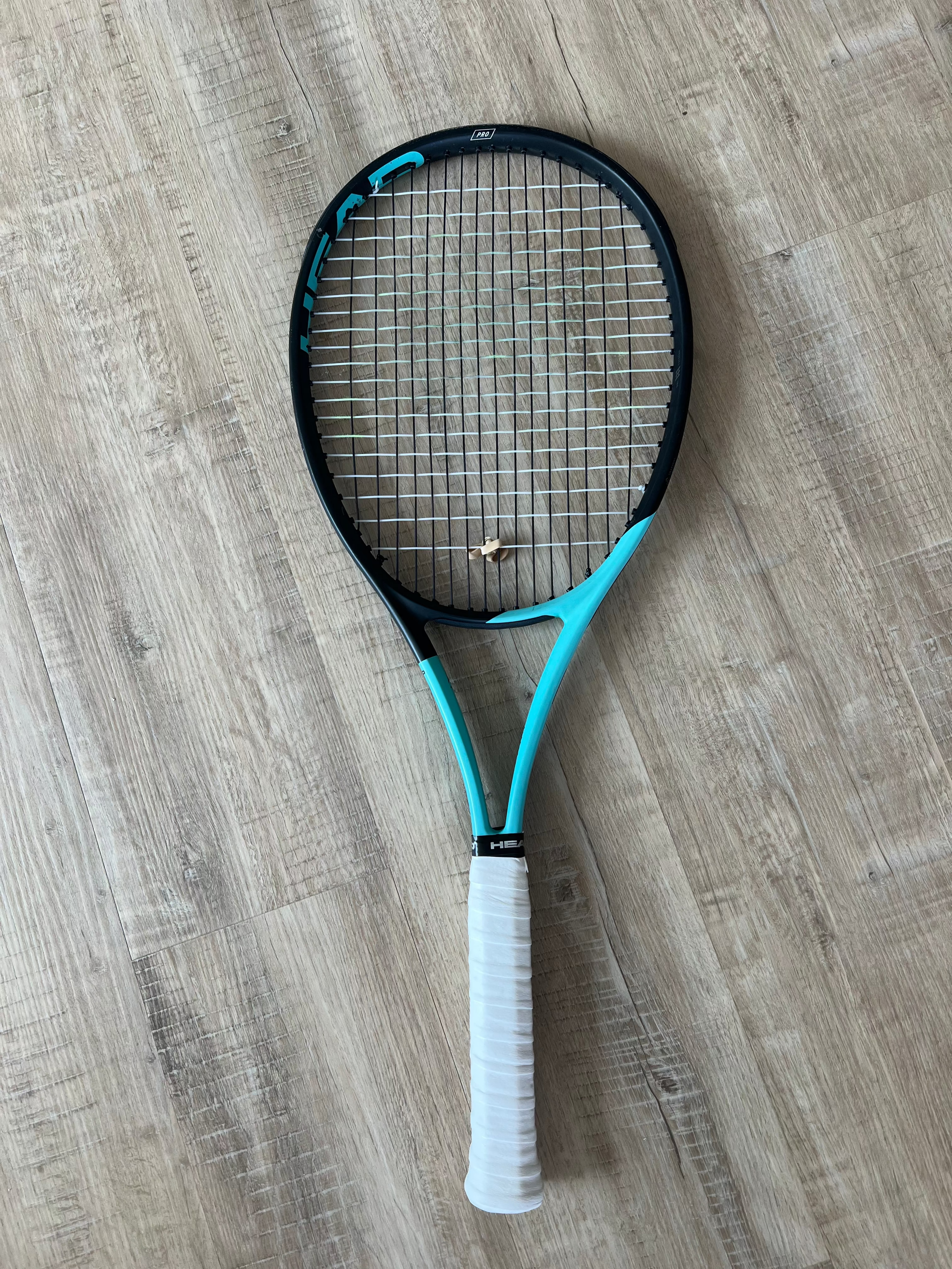A pre-owned Head Boom Pro 2022 tennis racquet by Head, featuring blue and black colors with a white grip, suited for advanced players, is placed on a light wood floor.