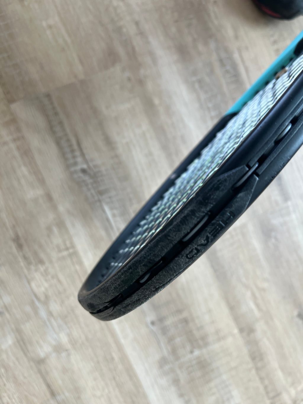 Close-up of a pre-owned Head Boom Pro 2022 (4 3/8) tennis racquet, highlighting wear on the black frame as it rests on a light wooden floor—perfect for advanced, intense players.