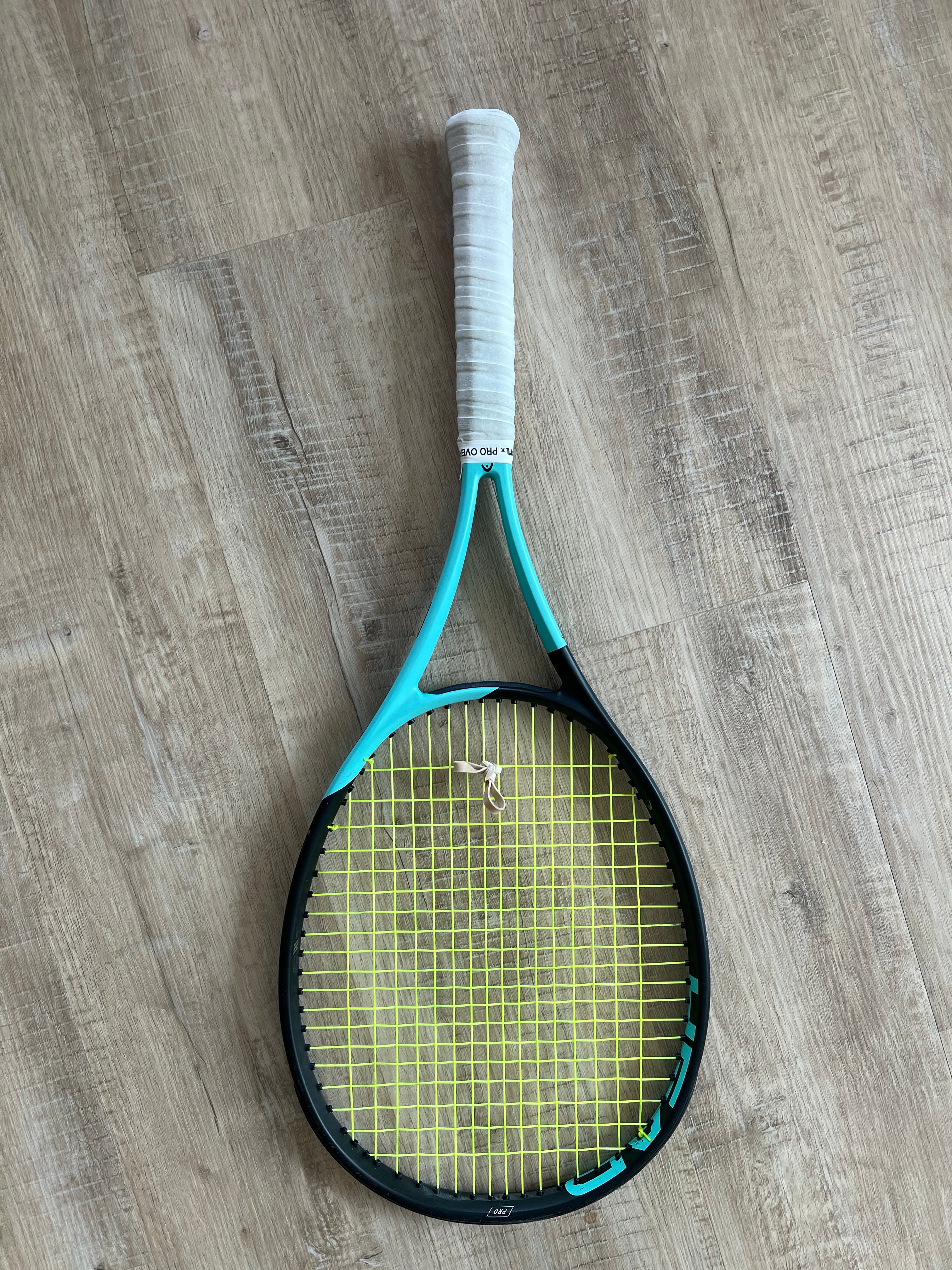 A pre-owned Head Boom Pro 2022 tennis racquet (4 1/4 grip) with a blue and black frame, yellow strings, and a white grip is shown on a wooden floor—ideal for players wanting power and control.