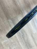 Close-up of the Head Boom Pro 2022 (Pre-Owned) 4 1/4 tennis racquet with yellow strings on a light wooden floor—perfect for aggressive players seeking precision.
