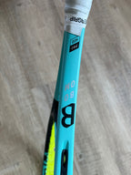 A close-up of a pre-owned Head Boom Pro 2022 (4 1/4) tennis racquet with “B OOM” and “PRO 400” on the frame, resting on a light wooden floor—ideal for aggressive players who want power and precision.