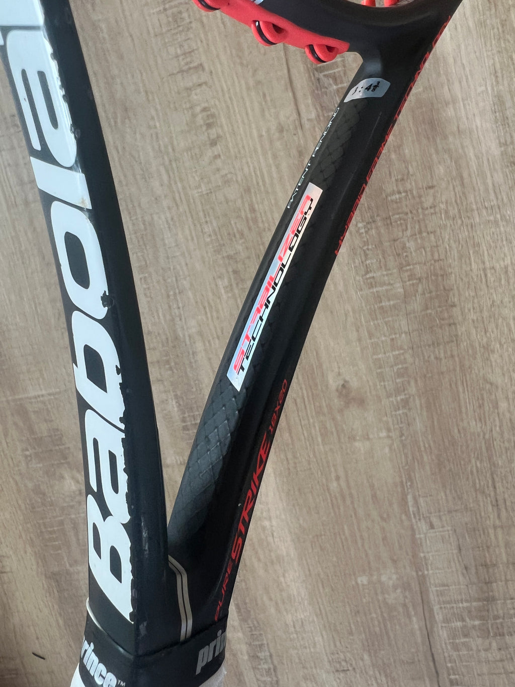 Close-up of a black Babolat tennis racquet with red accents and white branding, placed on a wooden surface.