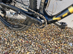 A close-up of the Specialized S-WORKS Epic - Large mountain bike drivetrain and pedal, resting on gravel by a beige wall.